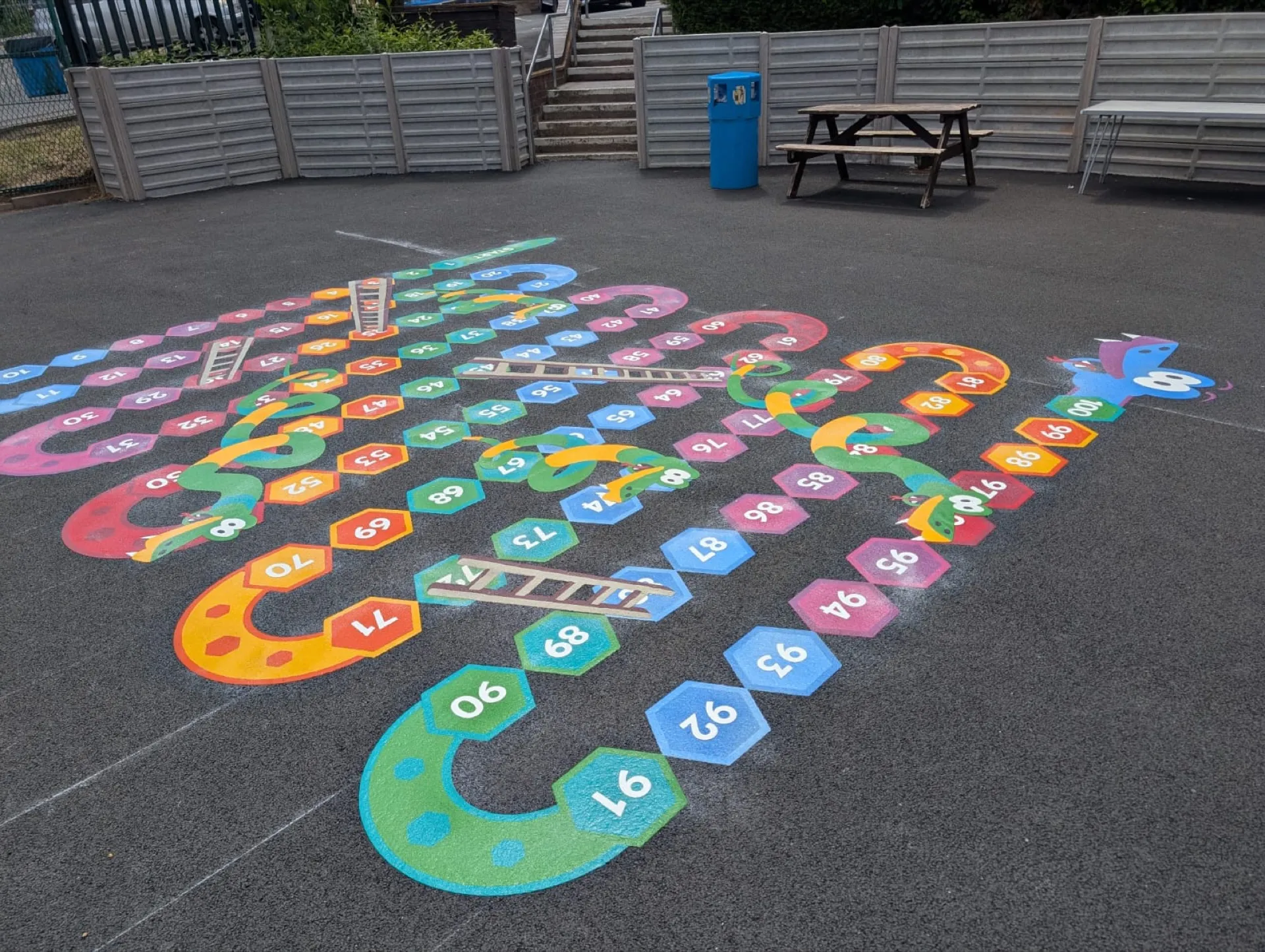 A big, colourful 3D snakes and ladders thermoplastic marking laid across a school playground
