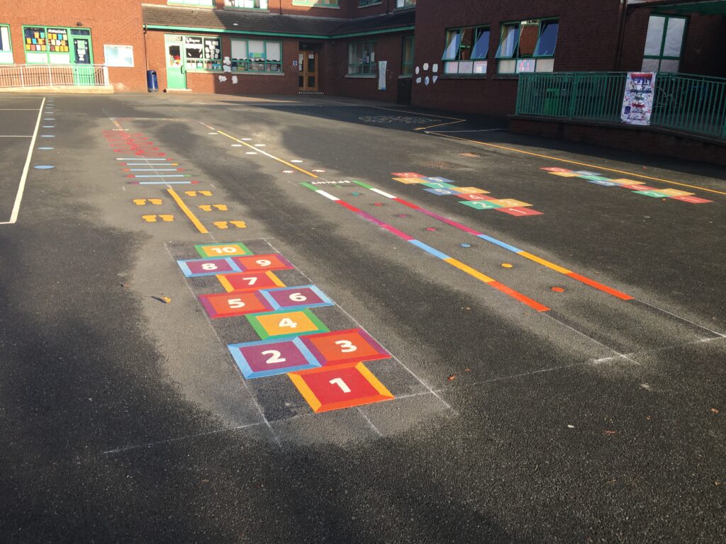 Square hopscotch, footprint trail and coloured running lines on a playground in low sun outside a red-brick school