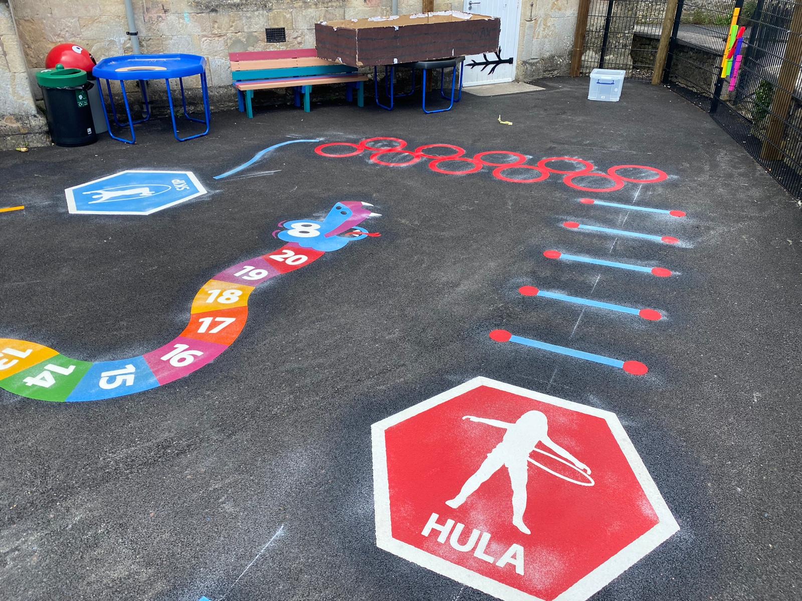 Hula and skip activity hexagons, a number snake and red hoop circles on new tarmac in a stone-walled yard